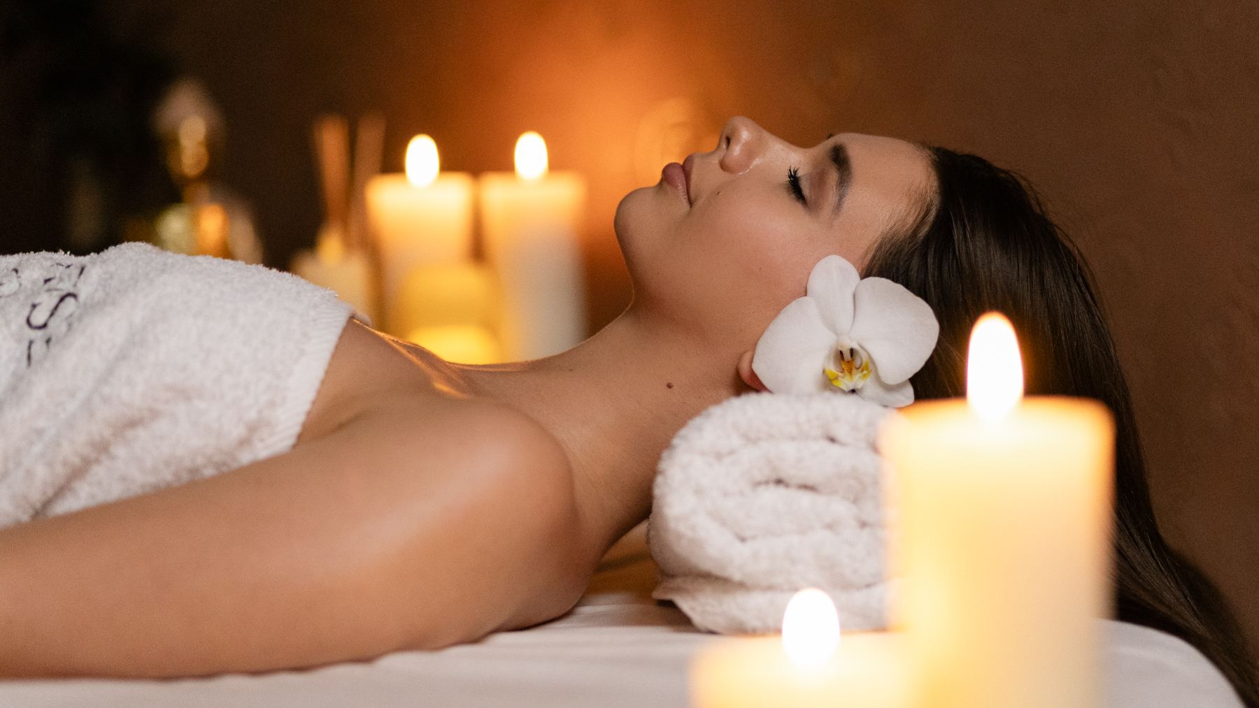Žena vdechuje vůni esenciálních olejů při aromaterapeutické masáži při svíčkách v salonu ESCAPE
